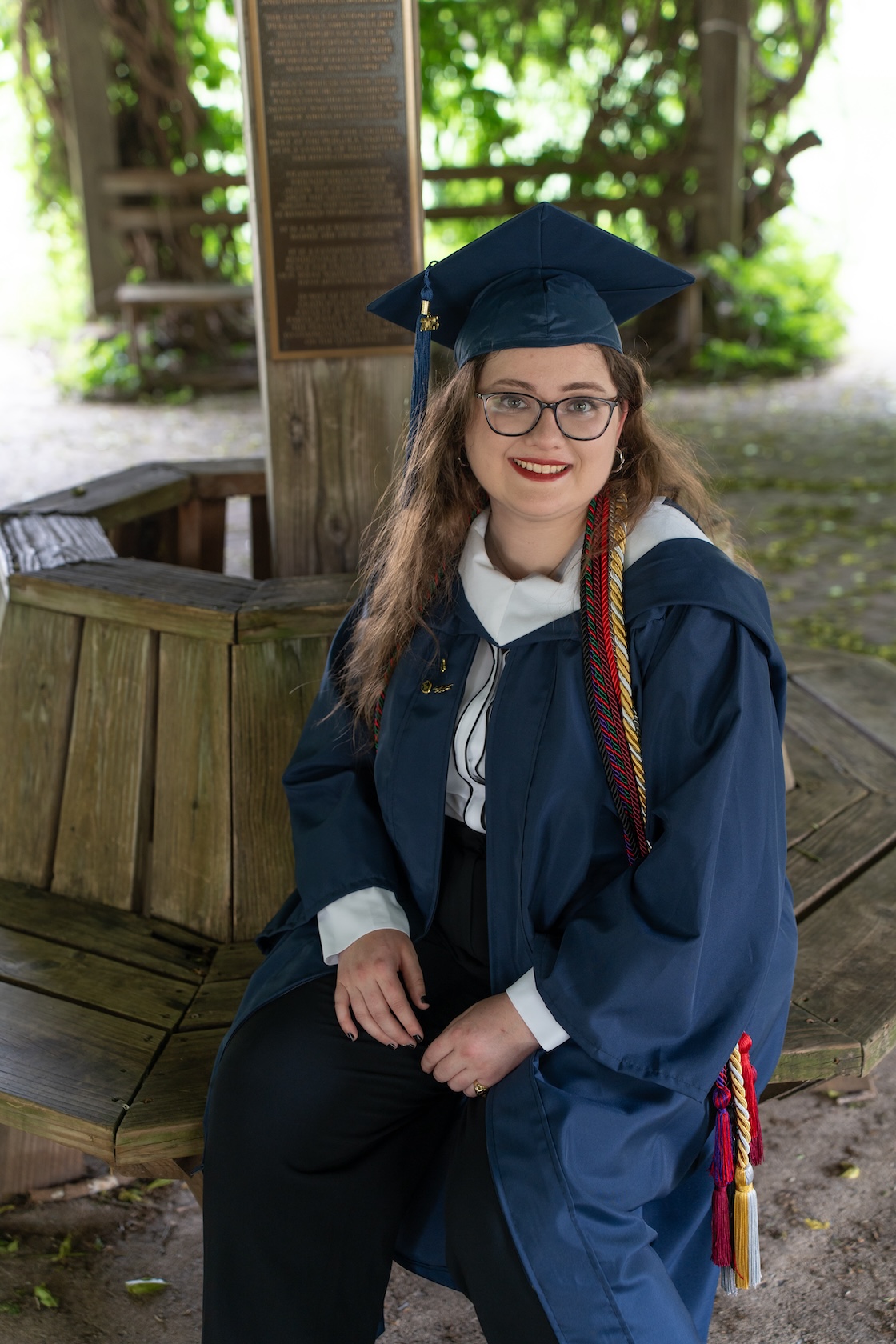 A photo of Rebecca Carroll wearing regalia while sitting in the Pergola on campus.
