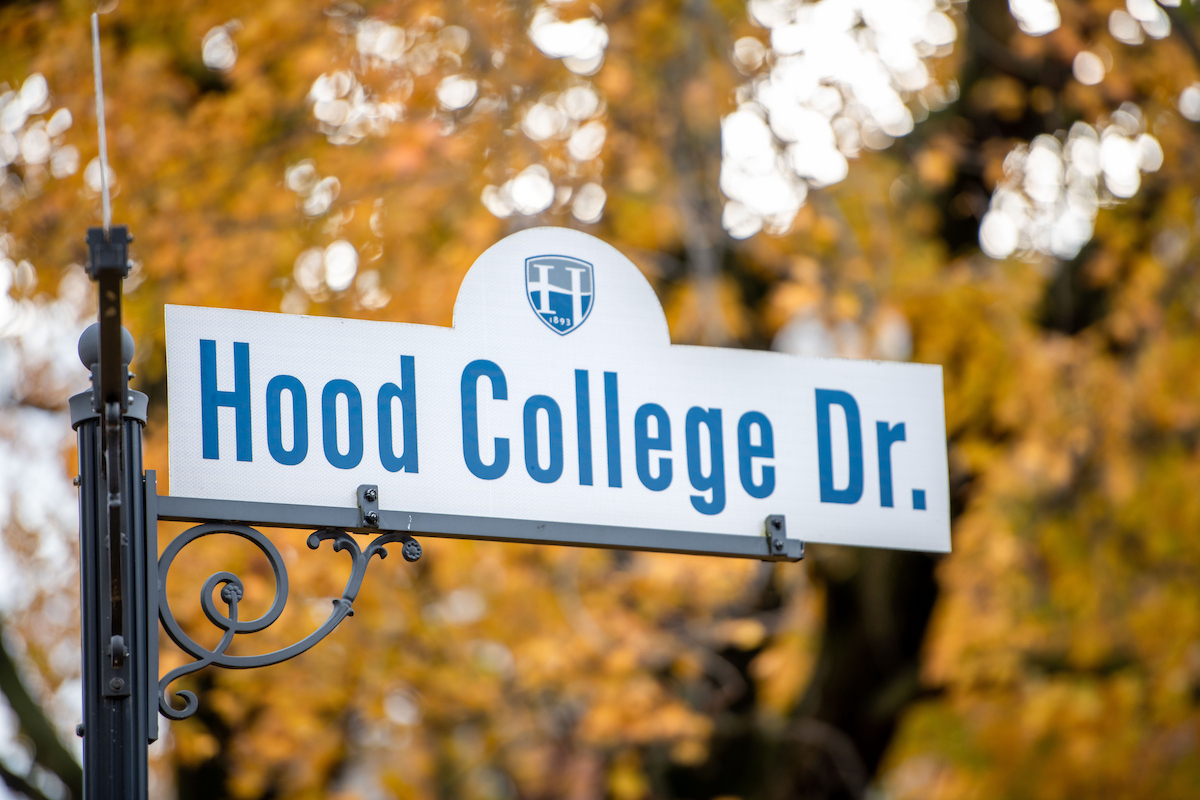A street sign reading "Hood College Drive" in front of a backdrop of orange foliage