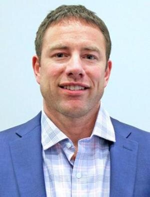 A headshot of coach Chad Dickman, wearing a blazer