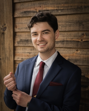 Professional headshot of Nathan Reese smiling with a navy blue suit, white shirt, and maroon tie/pocket square