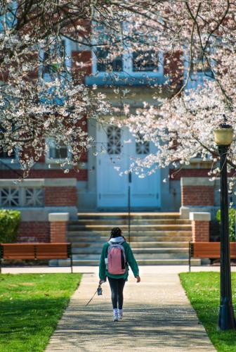 A Hood student wearing a backpack walks through campus towards Alumnae Hall