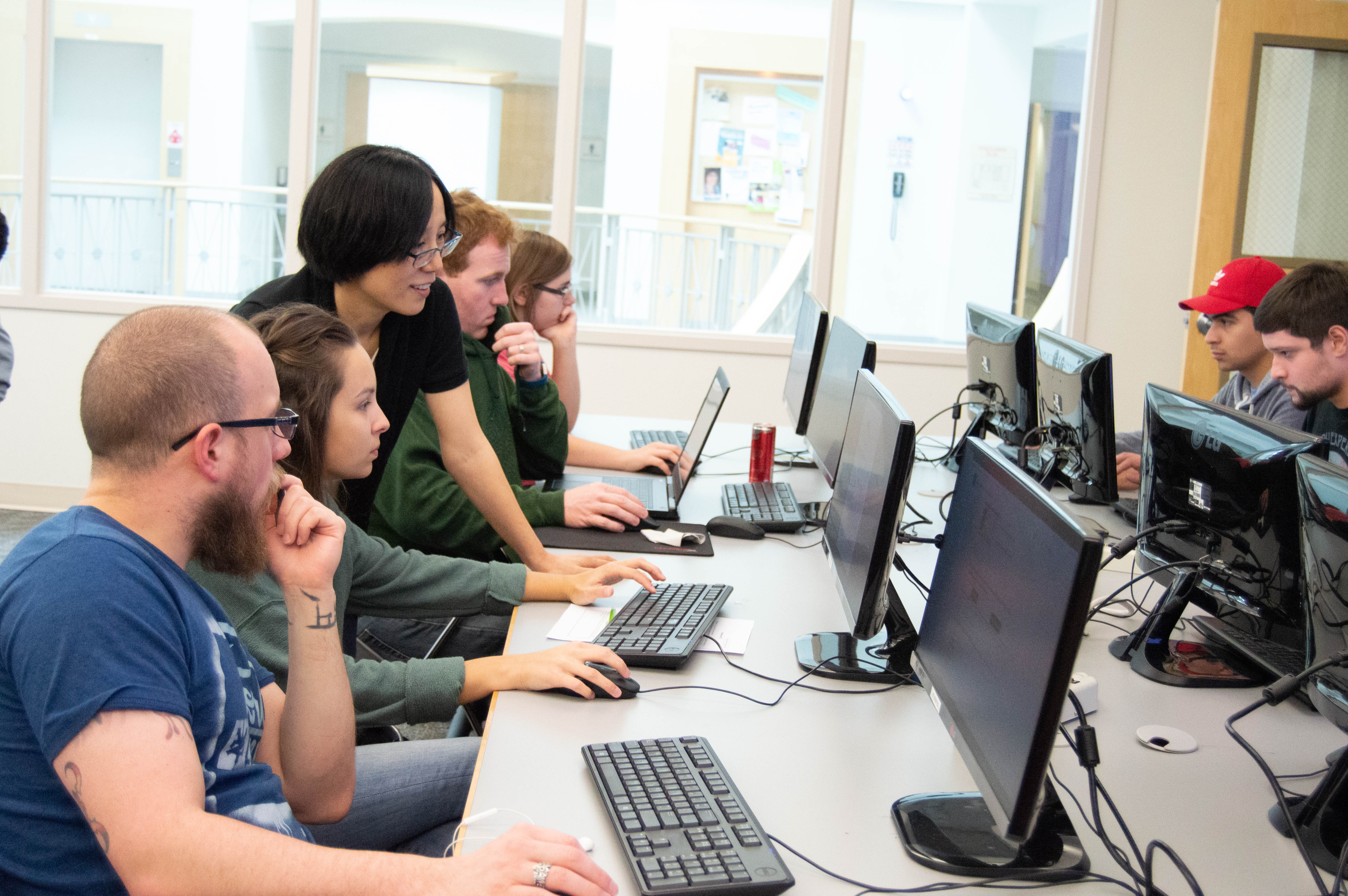 a classroom of students study a computer screen, with a professor instructing them