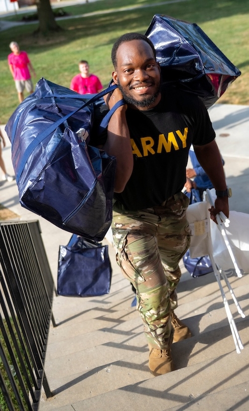 A move-in volunteer from the ROTC program helps carry items into Smith Hall