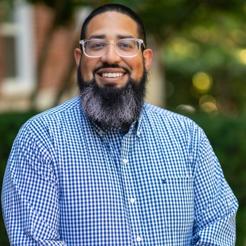 man with glasses and a beard wears a blue and white checked shirt